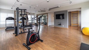 A spacious gym with various exercise equipment, wooden flooring, and a large mirror. - Akile Bela Vista Tatro Renault (São Paulo)