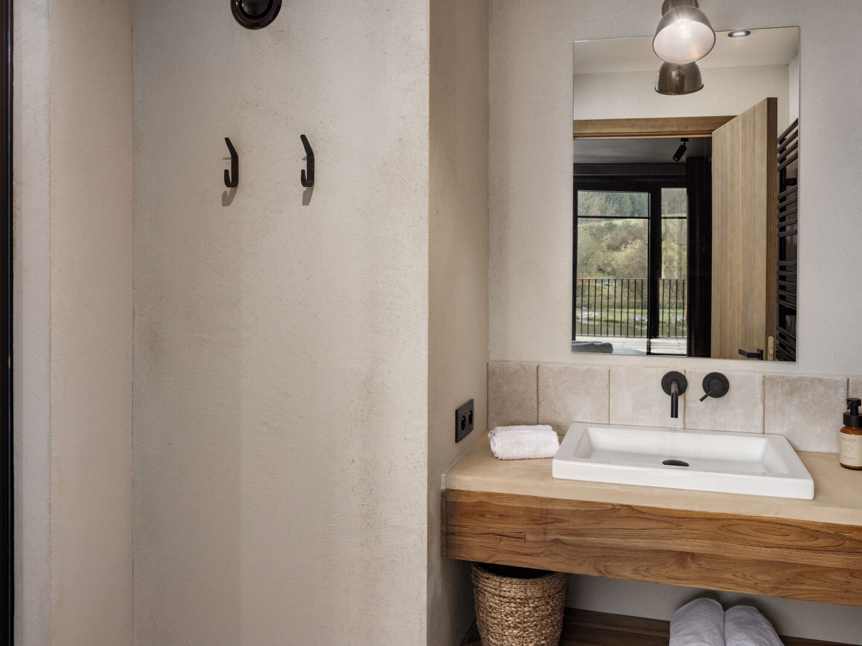 A bathroom with a wooden vanity, a white sink, a mirror, and a view of the outdoors.