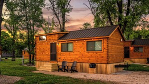 Eine Holzblockhütte mit Veranda, einer kleinen Terrasse und einem Grillplatz.