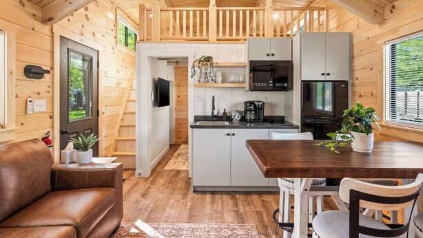Ein gemütliches Blockhaushaus-Interieur mit Holzvertäfelung, einer Küchenzeile mit modernen Geräten, einem Esstisch und einer komfortablen Sitzecke.