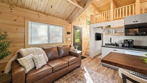 Un intérieur de chalet chaleureux avec un canapé en cuir marron, une cuisine équipée d’appareils modernes et des murs en bois.