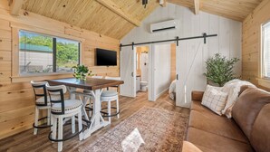 A cozy cabin interior with a wooden ceiling, a dining area with a table and chairs, a living room with a sofa, and a TV mounted on the wall. - Experience the timeless charm of the Pinecrest Cabin, a delightful twist on the classic cabin style. Step inside and be greeted by the warm and rustic log cabin ambiance that will transport you to the heart of Branson, MO. (Branson)