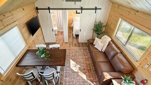 A cozy cabin interior with a dining area, a sofa, and a TV. - Experience the timeless charm of the Pinecrest Cabin, a delightful twist on the classic cabin style. Step inside and be greeted by the warm and rustic log cabin ambiance that will transport you to the heart of Branson, MO. (Branson)