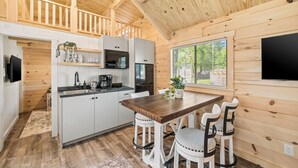 A modern kitchen with white cabinets, a wooden dining table, and bar stools. - Experience the timeless charm of the Pinecrest Cabin, a delightful twist on the classic cabin style. Step inside and be greeted by the warm and rustic log cabin ambiance that will transport you to the heart of Branson, MO. (Branson)