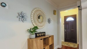 Un pasillo con una consola de madera, una planta en maceta, espejos decorativos en la pared y una puerta de madera oscura.