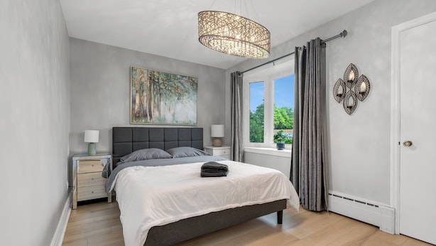 Un dormitorio con cama, mesitas de noche, un cuadro, una ventana con cortinas y un elemento decorativo en la pared.