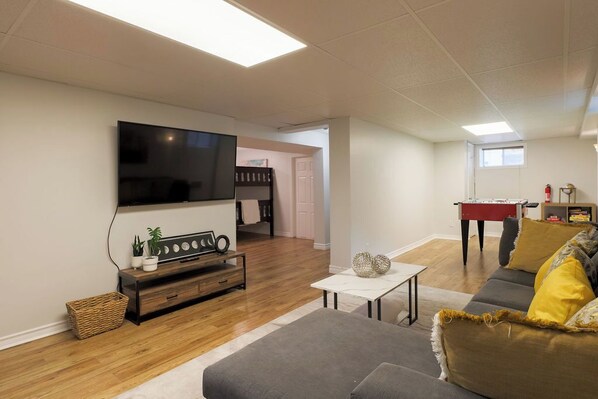 A living room with a flat-screen TV, a sofa, a coffee table, and a foosball table.