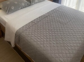 Een bed met een grijs gebogen sprei en een wit kussen met een bloemenprint.