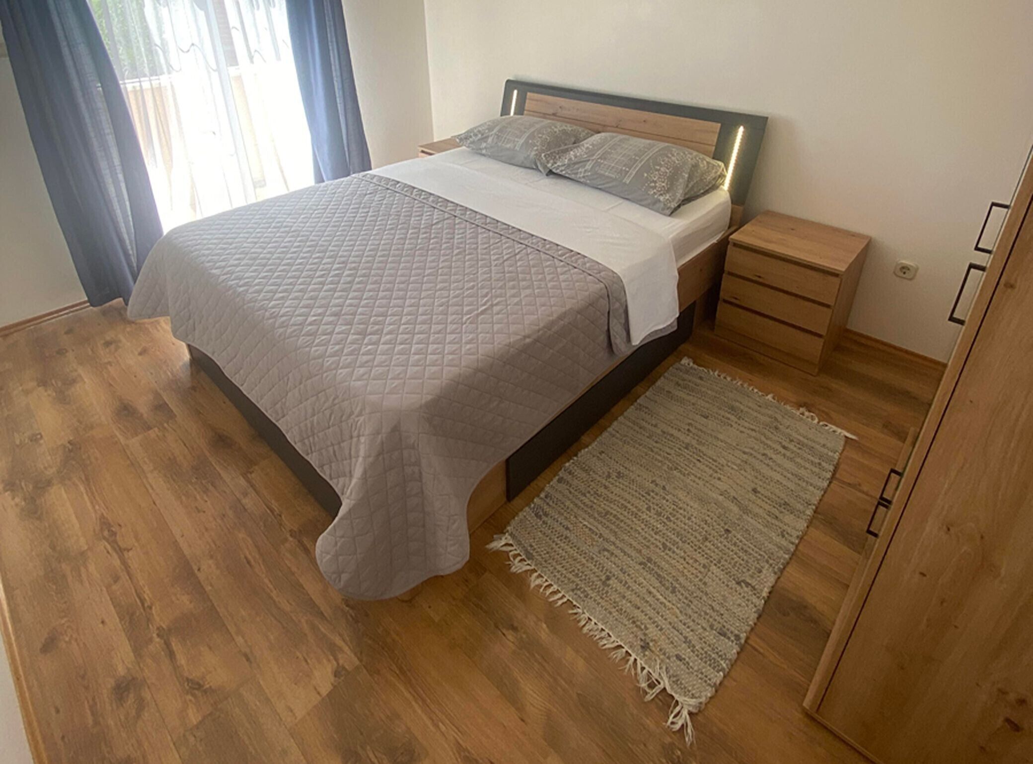 A bedroom with a bed, a nightstand, a wooden wardrobe, and a rug.