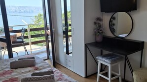 Une chambre avec un lit, un bureau, une chaise, une télévision et un balcon donnant sur l’eau.