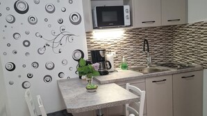 Une cuisine compacte équipée d’un four à micro-ondes, d’une machine à café et d’un évier. On y trouve une petite table avec des chaises et un mur décoratif orné de motifs circulaires.