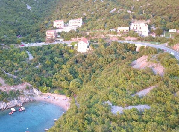A coastal village with buildings surrounded by dense greenery and a beach.