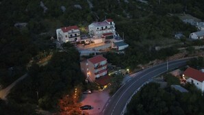 Un immeuble à plusieurs étages, doté d’un toit rouge et entouré de verdure, situé près d’une route sinueuse.