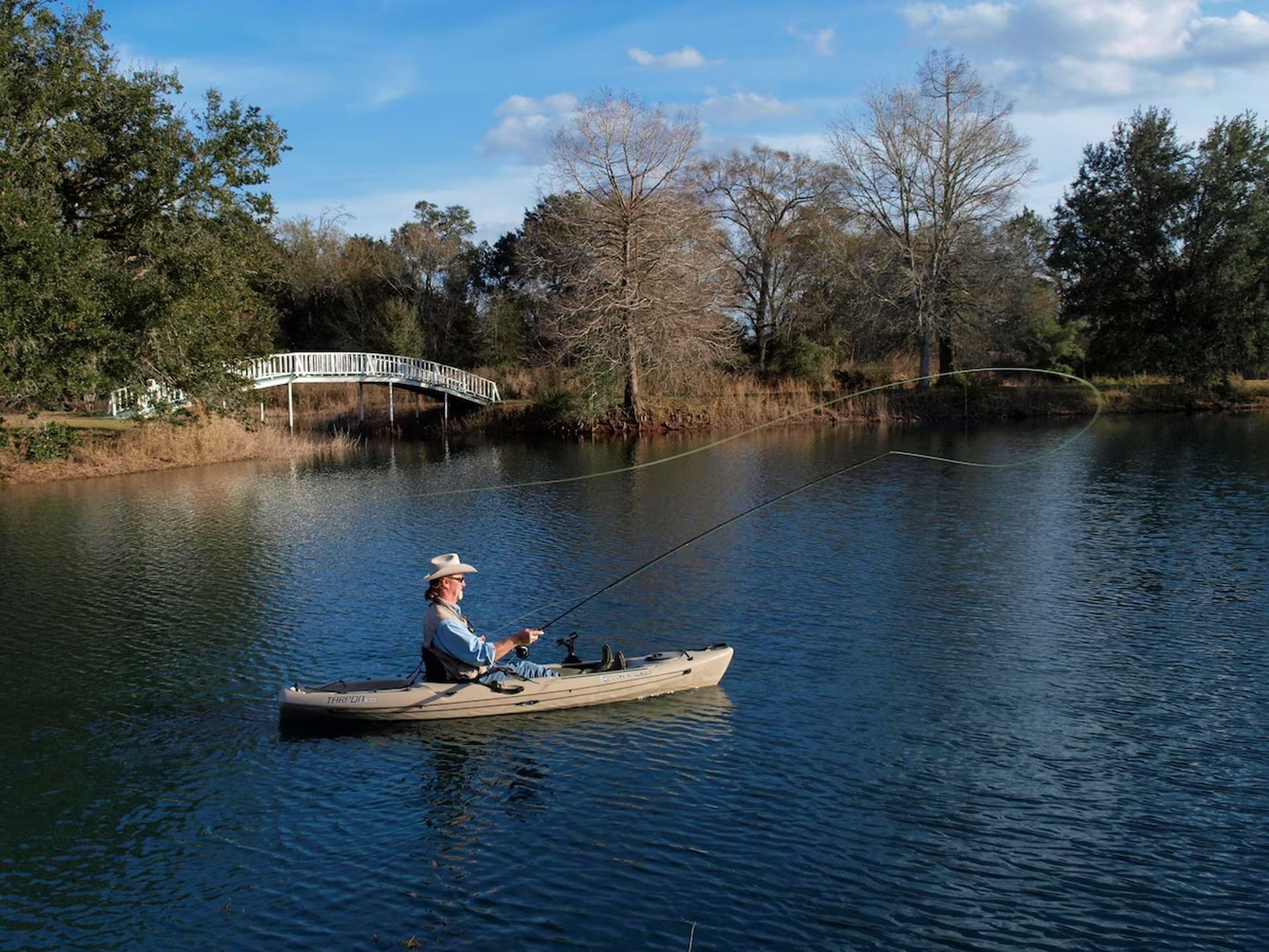 Una persona pescando desde un bote pequeño en un lago tranquilo, con un puente al fondo.