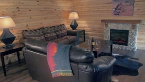 Een gezellig houten blokhut interieur met een leren bank, twee lampen, een open haard en een stenen schoorsteenmantel.