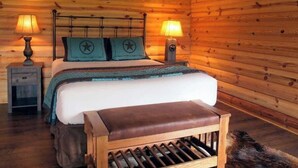 Een slaapkamer in een houten hutje met een bed, twee bedlampen, een nachtkastje en een bankje.
