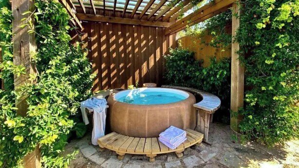Een hottub met een houten terras en een pergola erboven.