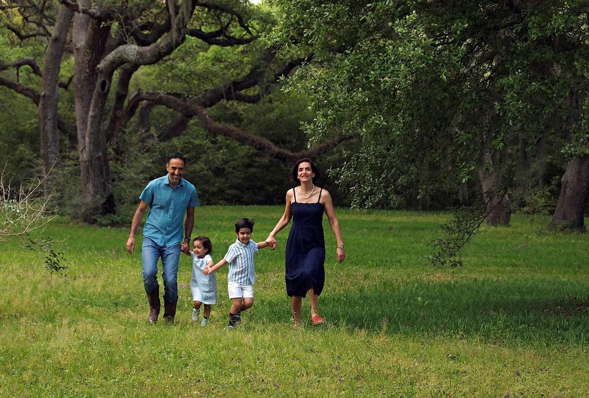 A family walking in a grassy field with trees in the background.
