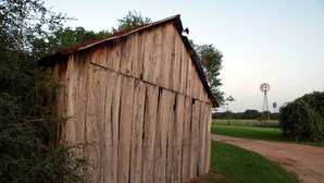 A rustic wooden barn with a metal roof, surrounded by greenery and a dirt path.