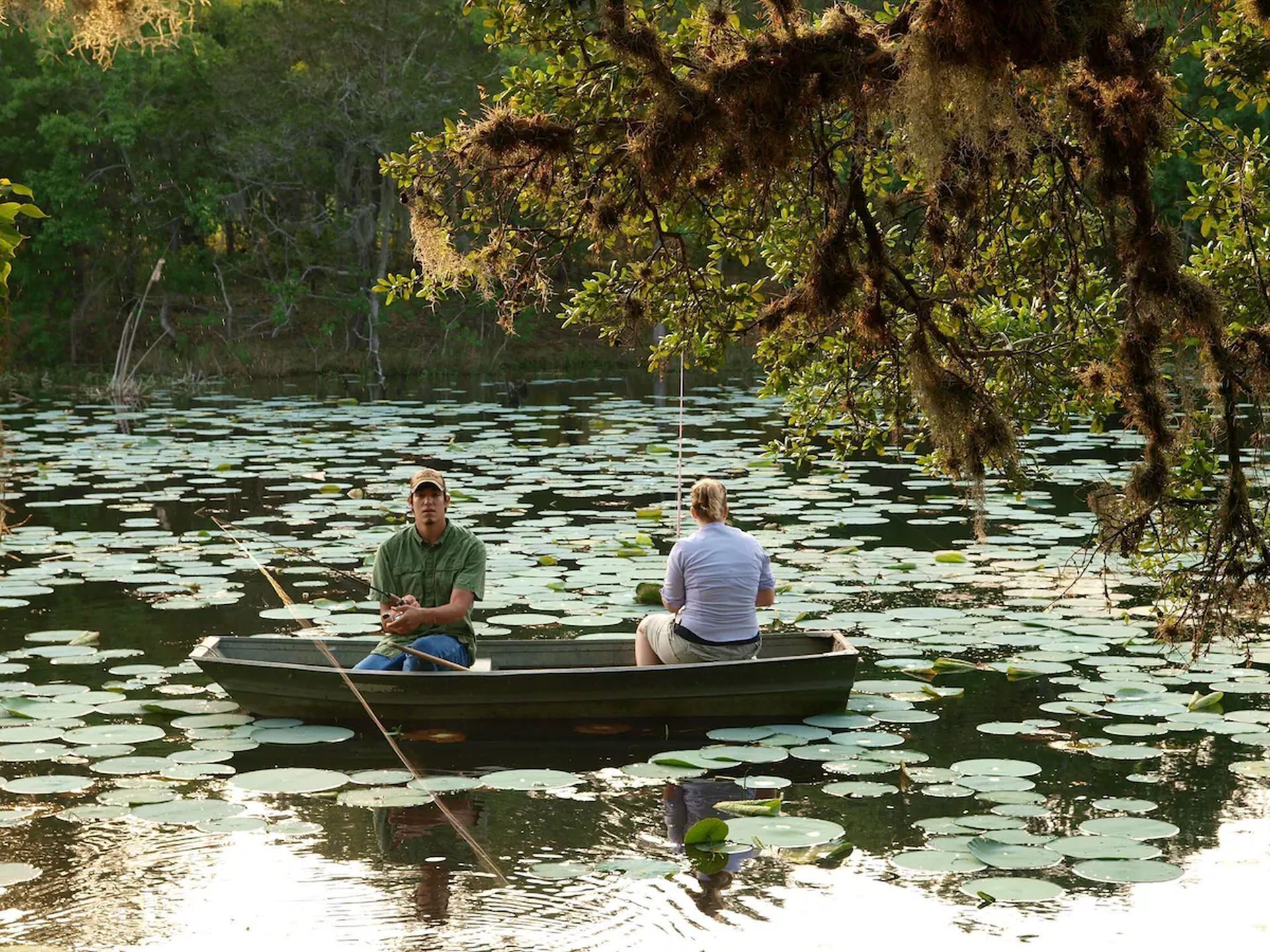 Two people in a small boat on a lake surrounded by lily pads.