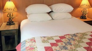 Een bed met witte kussens en een quilt met bloemenprint, afgezet door twee nachtkastjes met lampen.