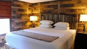 Una cama con sábanas y almohadas blancas, un cabecero de madera y dos lámparas de noche.