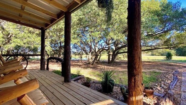 Una terraza de madera con bancos, rodeada de árboles y un césped.