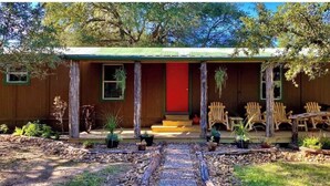Una cabaña rústica con puerta roja, porche de madera y mobiliario exterior.