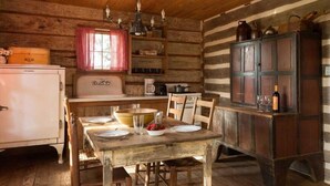 A rustic wooden cabin interior with a dining table set for two, a vintage refrigerator, and a wooden cabinet with doors. - 1800-style cedar Log Cabin on Blisswood Ranch with many optional activities! (Cat Spring)