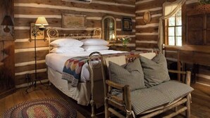 A log cabin room with a bed, a chair, a lamp, and a window. - 1800-style cedar Log Cabin on Blisswood Ranch with many optional activities! (Cat Spring)