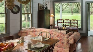 Un espace repas avec un banc incurvé, une table dressée pour deux personnes et une vue sur un espace extérieur verdoyant, visible à travers de grandes fenêtres.