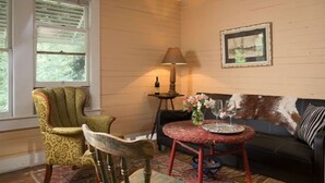 A cozy room with a patterned armchair, a vintage table with a lamp, and a sofa with a decorative throw. - Bluebonnet Bungalow with Private Hot Tub & options to enjoy fun Exotic Animal Safari! (Cat Spring)