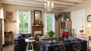 A cozy living room with floral-patterned sofas, a wooden coffee table, and a chandelier. - Texas Farm House getaway on BlissWood Ranch with Optional Activities & Safari! (Cat Spring)