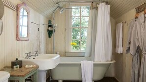 A bathroom with a clawfoot bathtub, a sink, a mirror, and a window with a view of greenery. - Texas Farm House getaway on BlissWood Ranch with Optional Activities & Safari! (Cat Spring)