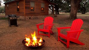 Une cabane en bois avec un foyer et deux chaises Adirondack rouges.