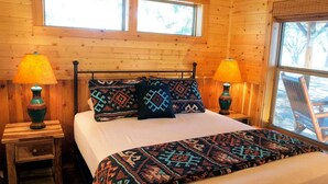 Une chambre à coucher dans une cabane en bois, avec un lit, deux tables de chevet, deux lampes et une fenêtre donnant sur la forêt.