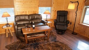 Une pièce chaleureuse avec un canapé en cuir, un fauteuil inclinable, une petite table avec des verres à vin et une bouteille, et deux lampes.