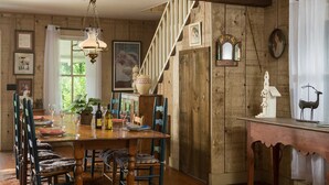 A wooden dining room with a large table set for six, surrounded by chairs. There is a staircase with a railing leading to an upper level. - Cozy Loft Suite-Part of Dog Trot House-Shared Pool, Fireplace Ranch Fun Options (Cat Spring)