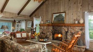 A cozy room with a stone fireplace, wooden furniture, and a view of the outdoors. - Cozy Loft Suite-Part of Dog Trot House-Shared Pool, Fireplace Ranch Fun Options (Cat Spring)