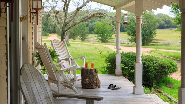 A porch with two rocking chairs, a wooden stump, and a pair of sandals. - Cozy Loft Suite-Part of Dog Trot House-Shared Pool, Fireplace Ranch Fun Options (Cat Spring)