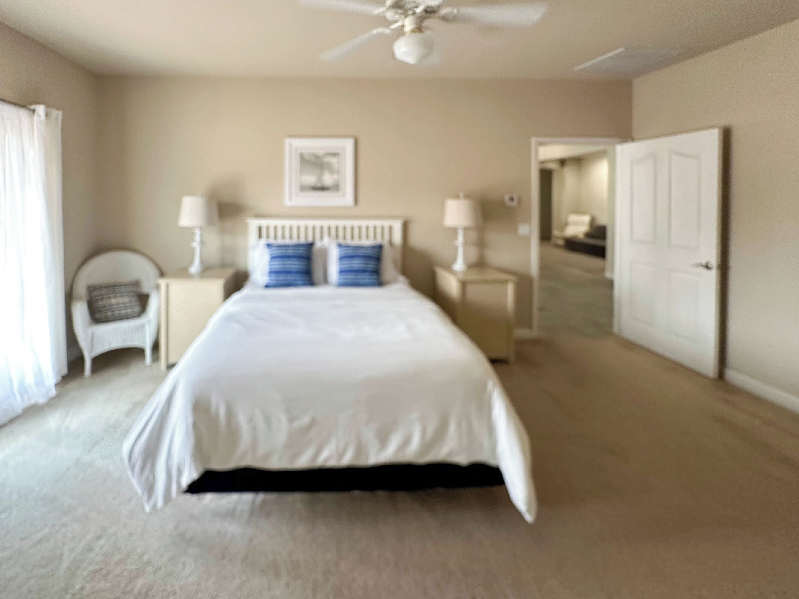 A bedroom with a bed, two nightstands, a chair, a ceiling fan, and a door.