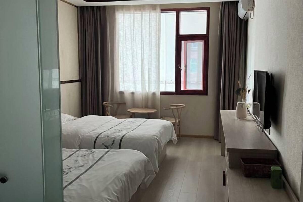 A hotel room with two beds, a small table, a TV, and a window with curtains.