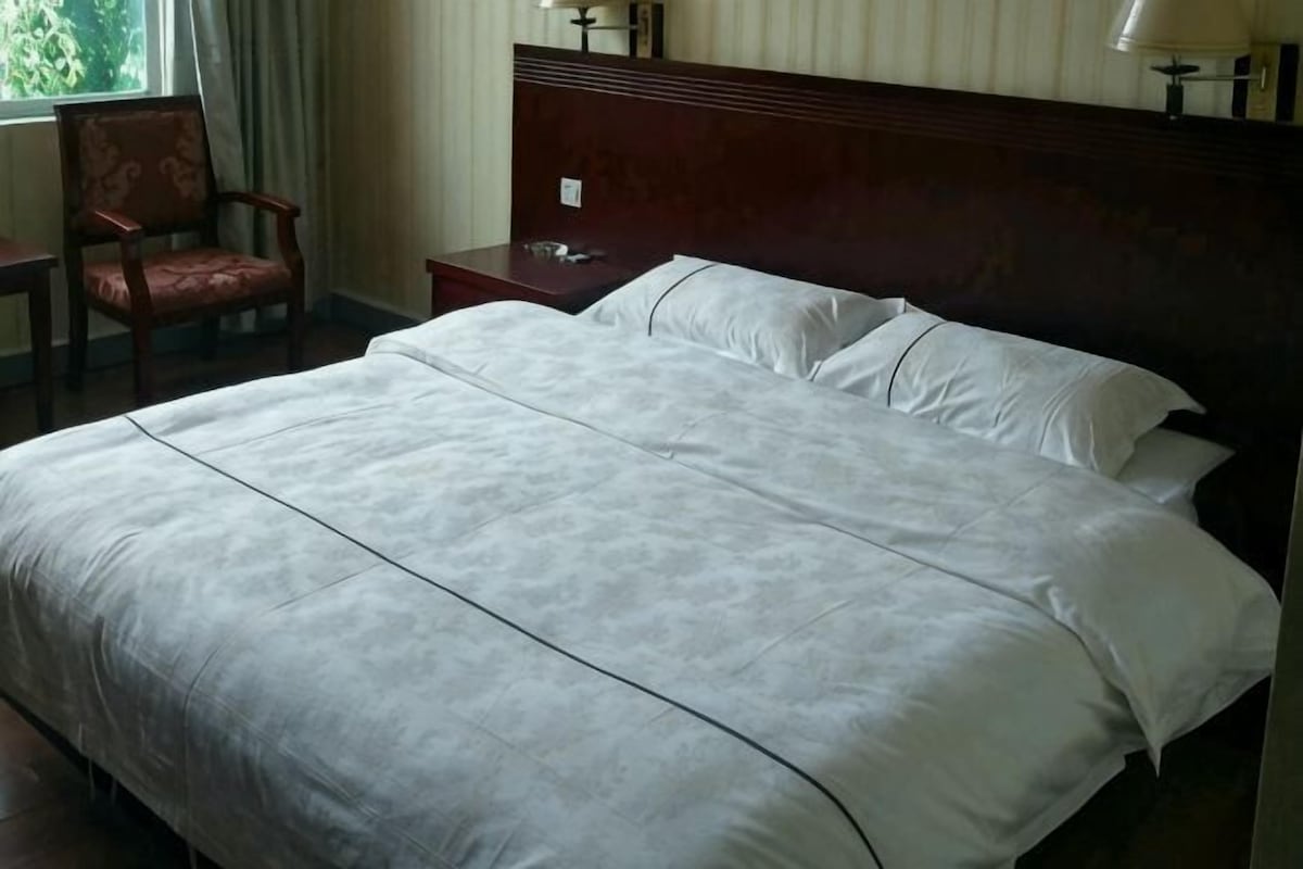 A hotel room with a large bed, a nightstand, a chair, and a window with curtains.