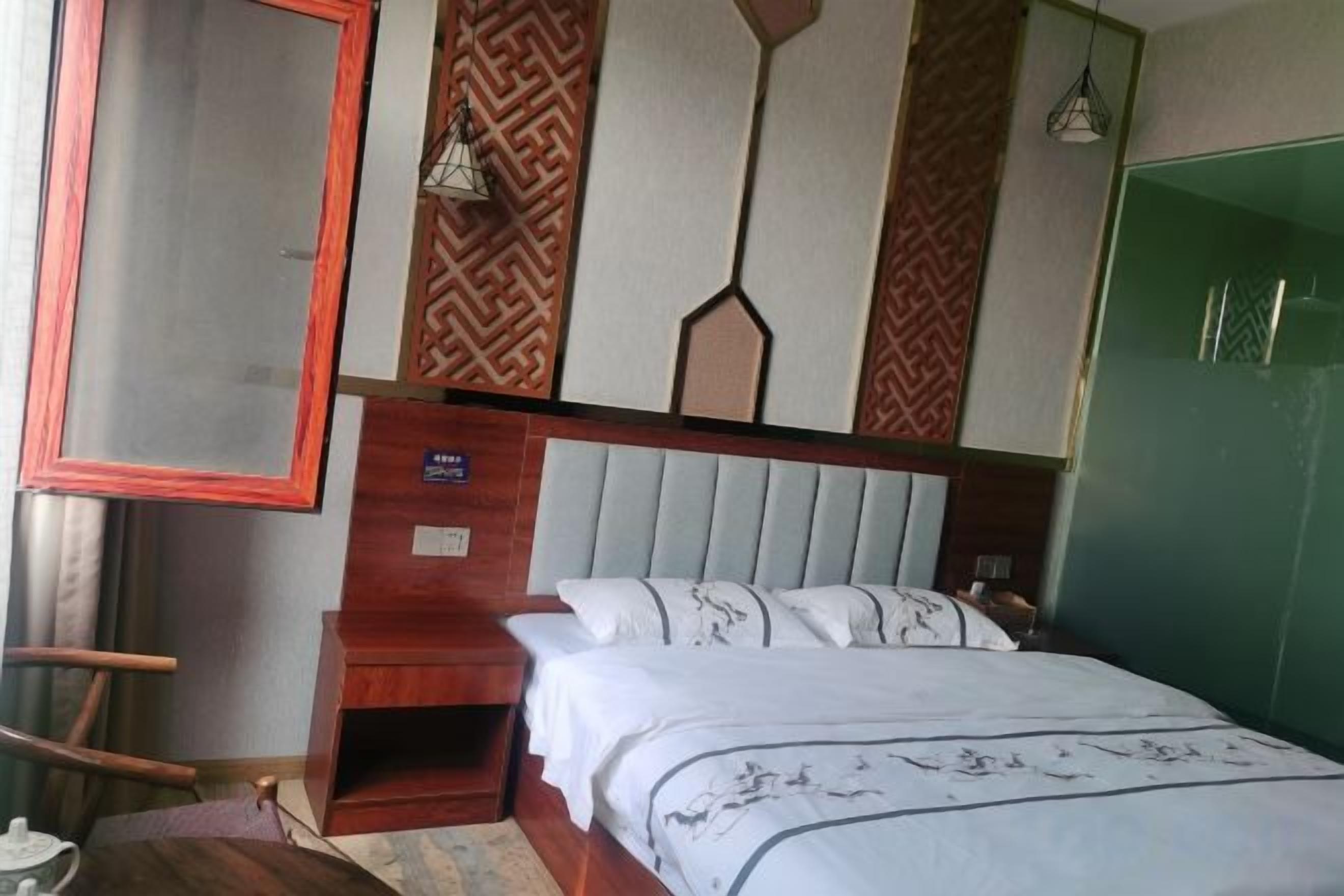A bedroom with a bed, a wooden nightstand, a green wardrobe, and a mirror on the wall.