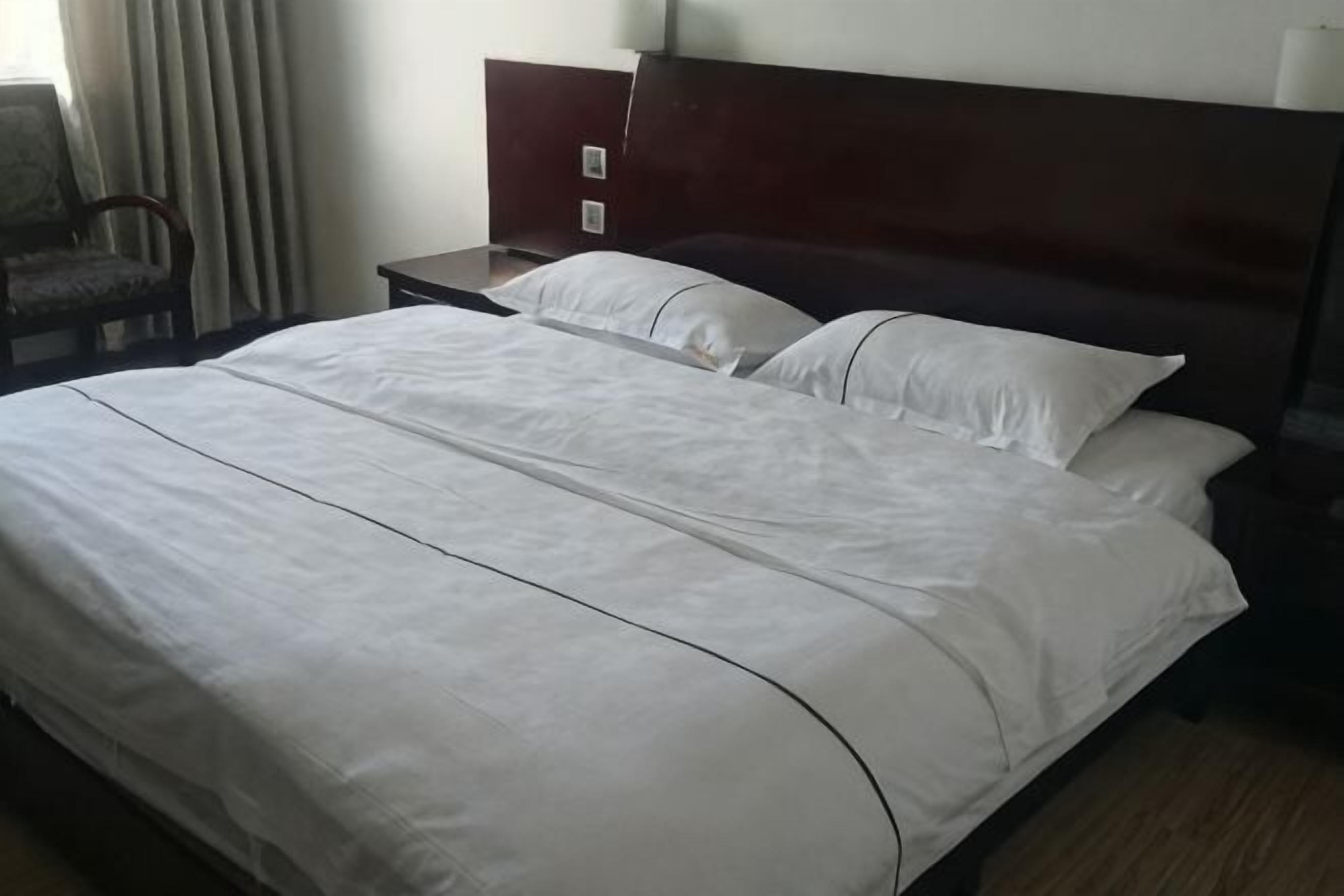 A neatly made bed with white linens, a wooden headboard, and a nightstand with a lamp.
