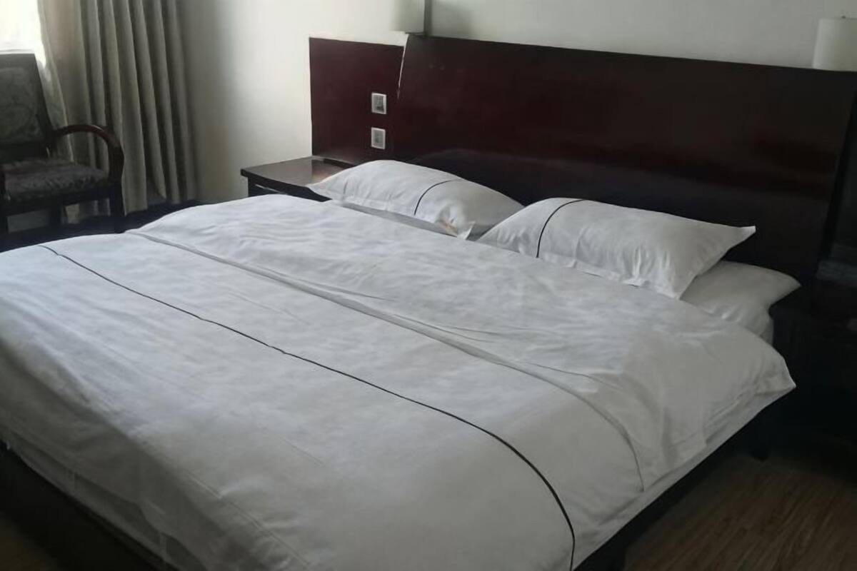 A neatly made bed with white linens, a wooden headboard, and a nightstand with a lamp.