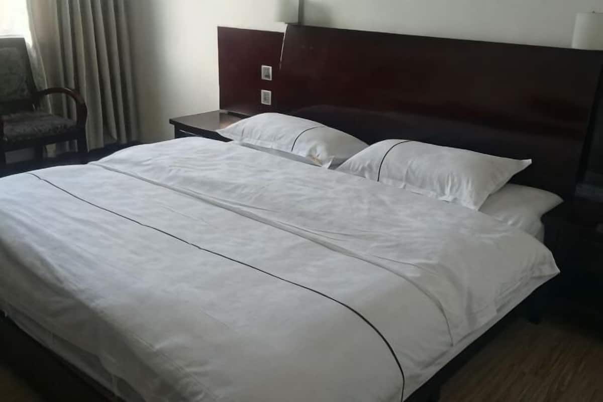 A neatly made bed with white linens, a wooden headboard, and a nightstand with a lamp.