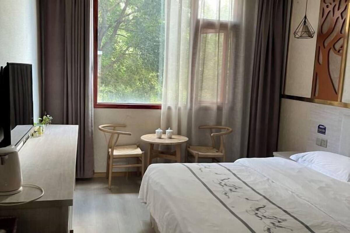 A hotel room with a bed, two chairs, a small table, a TV, and a window with curtains.