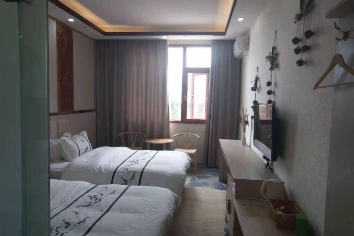 A hotel room with two beds, a desk, a chair, and a window with curtains.