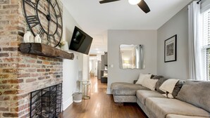 Ein modernes Wohnzimmer mit Kamin aus Ziegelsteinen, einem grauen Ecksofa und einem Wand-Fernseher.